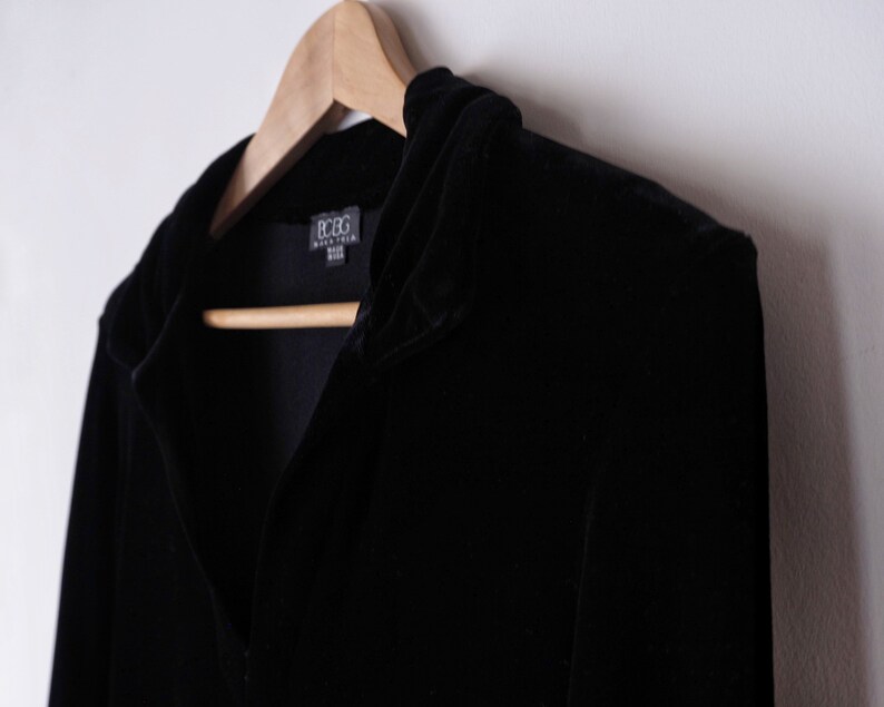 K&ouml;nnte beinhalten: Eine schwarze Samtjacke mit Kapuze und einem BCBG Max Azria-Etikett.