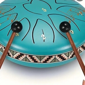 May include: A teal steel tongue drum with a patterned border and etched lines. The drum has numbers etched on the surface and is being played with two wooden mallets with black ball heads. Musical notes are illustrated above the drum.