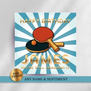 May include: A square greeting card featuring a blue and white sunburst background with a red and black table tennis paddle and ball. The text reads HAPPY BIRTHDAY JAMES YOU'RE STILL SMASHING IT in gold foil lettering. A gold foil seal says FOIL FINISH.