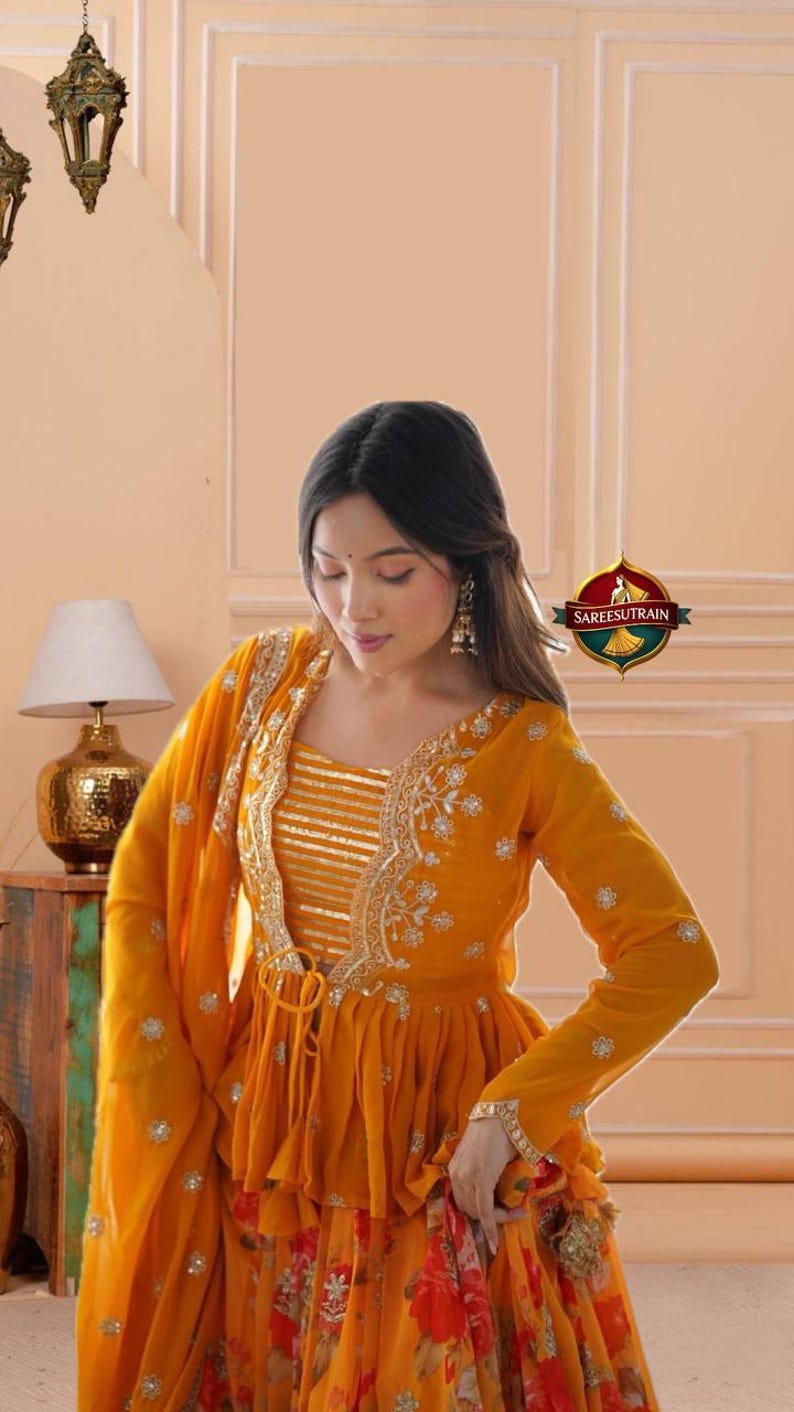 May include: A vibrant mustard yellow peplum-style top featuring long sleeves, a V-neckline, and intricate gold embroidery along the front edges. The bodice includes horizontal gold stripes, while the skirt displays a floral print in red and orange.