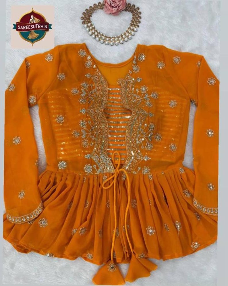 May include: A bright orange long-sleeved peplum blouse featuring intricate gold floral embroidery, a central panel with horizontal gold stripes, and a drawstring tie at the waist with tassel ends. A matching gold beaded necklace is positioned above.