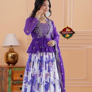 May include: A purple and white ensemble featuring a long-sleeved peplum jacket with silver embroidery over a striped bodice, paired with a floor-length skirt displaying a purple floral print and a matching purple dupatta with a silver border.