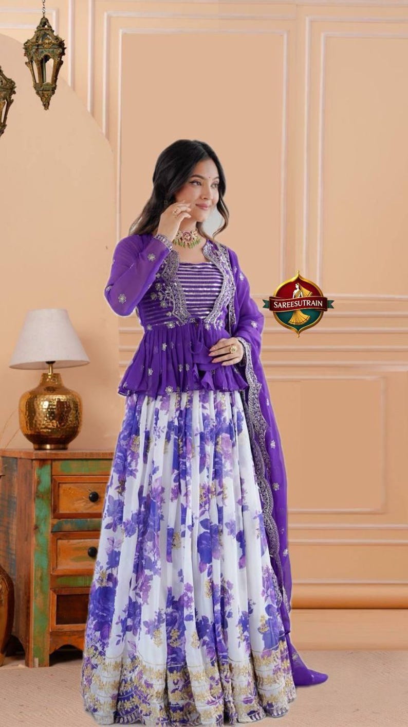 May include: A purple and white ensemble featuring a long-sleeved peplum jacket with silver embroidery over a striped bodice, paired with a floor-length skirt displaying a purple floral print and a matching purple dupatta with a silver border.