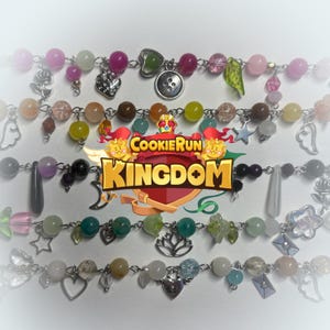 Op de afbeelding: Verschillende kettingen met kralen en diverse bedels, waaronder harten, sterren en bladeren. De kralen zijn in tinten roze, groen en transparant. De kettingen bevatten ook het logo "Cookie Run Kingdom".