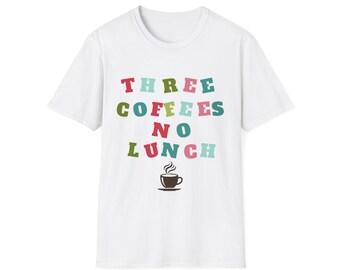 May include: A white short-sleeved t-shirt featuring the text "THREE COFFEES NO LUNCH" printed in a multi-colored block font. Below the text is a small, dark brown graphic of a steaming coffee cup on a saucer, centered on the chest area.