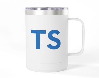 Può includere: Una tazza da viaggio in acciaio inossidabile bianco con manico e coperchio trasparente. La parte anteriore della tazza presenta le lettere TS stampate in un carattere sans-serif blu e grassetto. La tazza ha un corpo cilindrico e un bordo.
