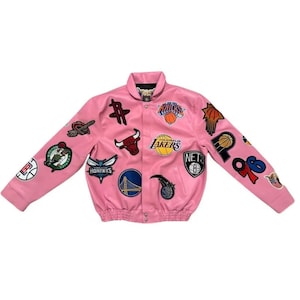 May include: Pink satin bomber jacket adorned with various NBA team logos and patches. Features a button-up front, ribbed cuffs, and a classic collar. The jacket showcases logos from teams like the Lakers, Celtics, and Hornets.