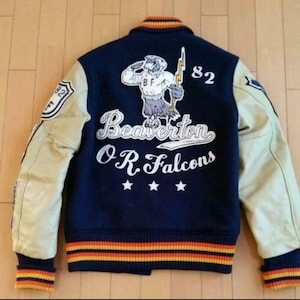 以下が含まれることがあります： 「Beaverton O.R. Falcons」の文字と、ファルコンのマスコットグラフィックが特徴の、ネイビーブルーとタン色のレターマンジャケット。ジャケットはタン色の袖、ストライプの襟、袖口、裾、そして数字の「82」が特徴です。