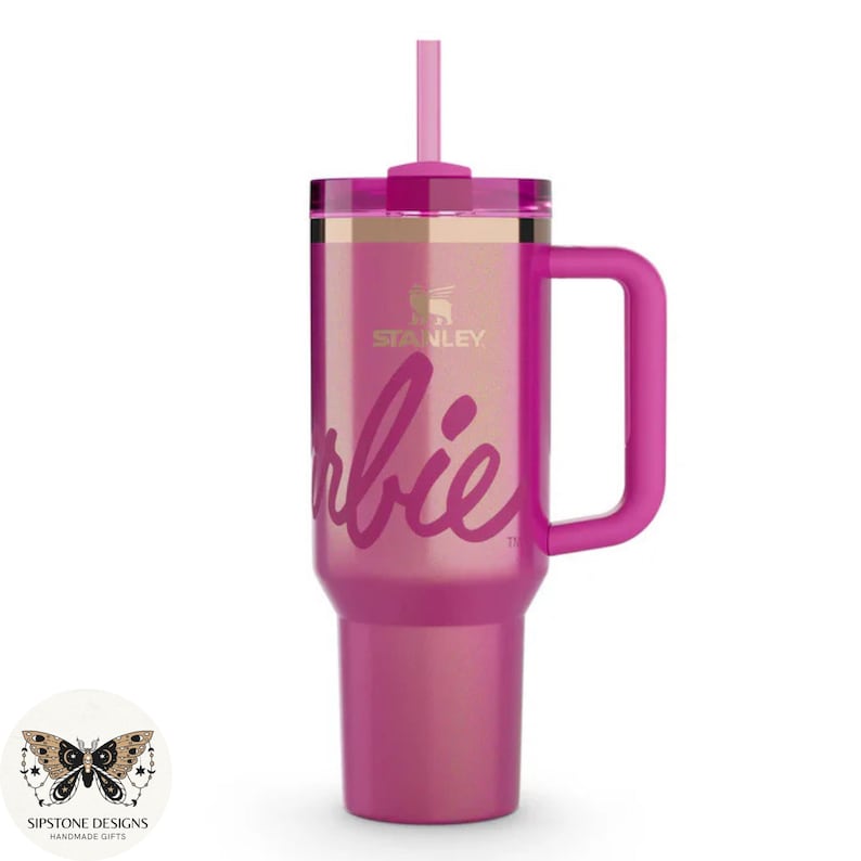 May include: A pink Stanley tumbler with a handle and straw. The word "Barbie" is written in cursive on the front. The Stanley logo is visible above the word "Barbie".