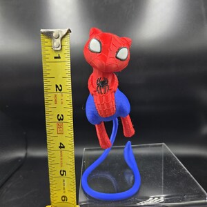 May include: A red and blue 3D-printed Spider-Man cat figurine. The figurine is approximately 5 inches tall. The cat has white eyes and a black spider emblem on its chest. A blue tail extends from the figurine.