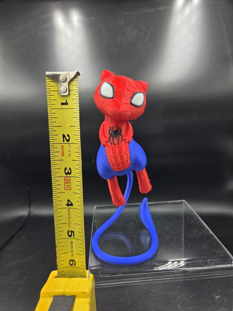 May include: A red and blue 3D-printed Spider-Man cat figurine. The figurine is approximately 5 inches tall. The cat has white eyes and a black spider emblem on its chest. A blue tail extends from the figurine.