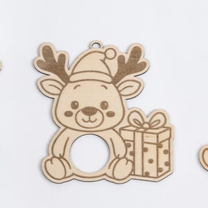 Puede incluir: Tres adornos navide&ntilde;os de madera con forma de reno. Cada reno tiene una abertura circular en el centro. Un reno tiene cuernos, uno tiene un gorro de Pap&aacute; Noel y un regalo, y el tercero tiene un gorro y una bufanda. El texto "DIGITAL PRODUCT ONLY!" est&aacute; en la esquina superior derecha.