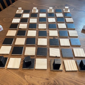 May include: A wooden board game with a checkerboard pattern of black and natural wood squares. The game includes black and natural wood game pieces and two dice with white backgrounds and red dots. The game is set on a wooden table.