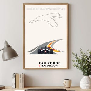 May include: A framed poster with a minimalist design of the Circuit de Spa-Francorchamps. The poster shows a race car on a curved track with red and yellow detailing, and the text "EAU ROUGE & RAIDILLON".