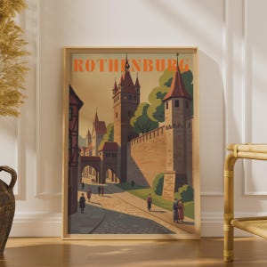 May include: A framed wall art print featuring a stylised illustration of the town of Rothenburg. The image depicts medieval stone towers, a city wall, and cobblestone streets with small figures walking. The word ROTHENBURG is printed in orange.