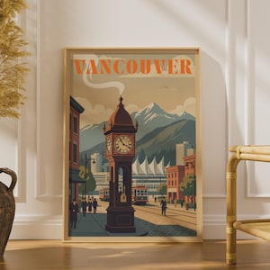 May include: A framed travel poster featuring the text VANCOUVER in orange letters at the top. The illustration depicts a steam clock in the foreground, city buildings, streetcars, and snow-capped mountains in the background under a soft sky.