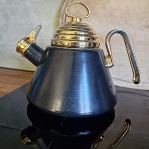 Könnte beinhalten: Ein dunkelblauer Herd-Wasserkessel mit konischem Körper, ausgestattet mit einem polierten, goldfarbenen Deckel im gerippten Bienenkorb-Design sowie einem passenden goldfarbenen Griff und Ausgusskappe. Der Kessel hat einen breiten Boden.