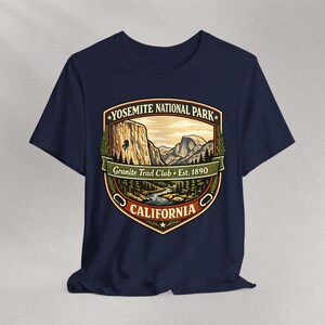 May include: Navy blue t-shirt featuring a Yosemite National Park graphic. The design includes a mountain landscape, river, and the text "Yosemite National Park, Granite Trad Club, Est. 1890, California". The graphic is in shades of green, brown, and beige.