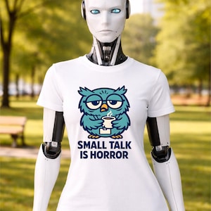 May include: White t-shirt featuring a cartoon owl with glasses holding a coffee cup. The owl is blue and teal, with the text "SMALL TALK IS HORROR" below. The shirt is worn by a white robotic figure.