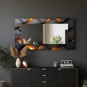 Può includere: Uno specchio da parete rettangolare con una cornice dal design geometrico nero e oro. Lo specchio è montato sopra un mobile nero con ferramenta dorata. Un orologio digitale mostra l'ora 10:09.