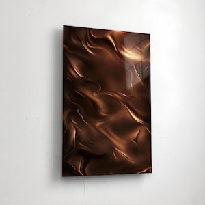 Può includere: Un'opera d'arte astratta rettangolare con finitura lucida. L'opera presenta un design ondulato e fluido in tonalità marroni e oro, creando un senso di profondità e movimento. L'opera è montata su una parete bianca.