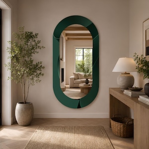 May include: A large, oval-shaped wall mirror featuring a wide, dark forest green frame with a smooth, curved, and layered design. The mirror is mounted on a light-colored wall, reflecting a bright living room space with a sofa and a fireplace.