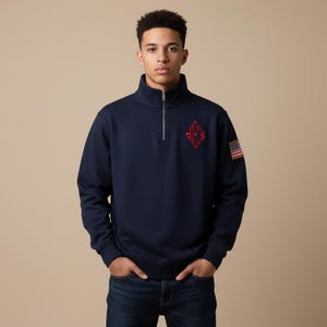 Puede incluir: Sudadera azul marino con cremallera de cuarto de cuello, con un emblema rojo bordado en el pecho y un pequeño parche de la bandera estadounidense en la manga. La sudadera tiene un cuello alto.