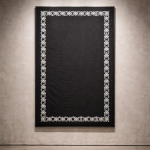 Peut inclure: Une œuvre d'art textile encadrée en noir avec une bordure en dentelle florale blanche. L'œuvre rectangulaire est accrochée à un mur de ton neutre. L'éclairage de piste au plafond illumine l'œuvre.