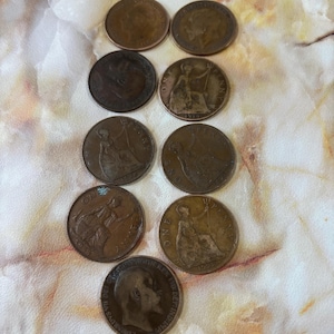 May include: A collection of antique British penny coins, featuring various designs and portraits. The coins are arranged on a patterned surface, showcasing their aged copper color and historical significance.