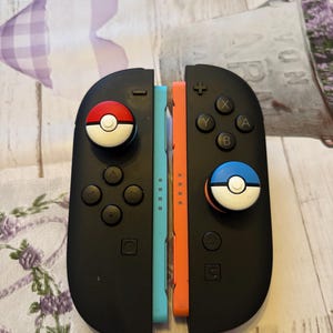 May include: Black game controllers with blue and orange sides. The controllers have a red and white Pokeball design on one side and a blue and white Pokeball design on the other. The controllers have buttons and directional pads.
