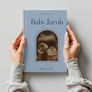 May include: A light blue hardcover book titled Letters to Baby Jacob with a central arched frame containing a sepia-toned ultrasound image. The text below the image reads DUE March 2027 in dark blue lettering on the front cover.
