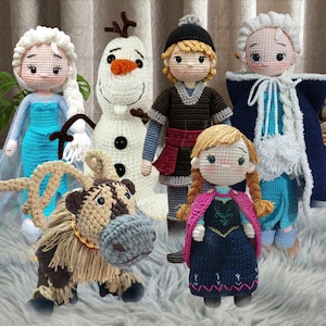 May include: A collection of five handmade crochet dolls representing characters from a popular animated film. The set includes two figures with blonde braided hair in blue dresses, a white snowman, a reindeer, and a figure in a dark tunic.