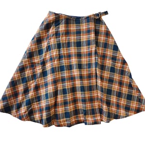 Pode incluir: Saia envelope xadrez em tons de azul marinho, laranja e creme. A saia apresenta um padrão xadrez clássico e um fecho de fivela na cintura. A saia tem uma silhueta rodada.