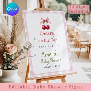 Puede incluir: Un letrero de baby shower sobre un caballete de madera. El letrero tiene un borde de cuadros rosas y presenta el texto "Cherry on the Top" y "Amelia's Baby Shower". También se muestra la fecha 14 de agosto de 2026. El letrero incluye un gráfico de cerezas y las palabras "12 Signs Included".