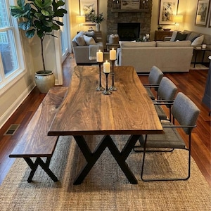 May include: A substantial dining table made of dark wood, with a matching bench and black metal legs. Grey upholstered chairs surround the table, which is set on a woven rug. Candles in black holders are on the table.