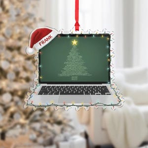 May include: A clear acrylic Christmas ornament shaped like a laptop with a Santa hat that says "FRANK". The laptop screen displays a Christmas tree made of code. The ornament is outlined with colorful Christmas lights and has a red ribbon for hanging.