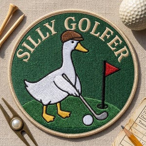 May include: A circular embroidered patch featuring a white goose wearing a brown cap, holding a golf club, and standing on a green field with a red flag and a white golf ball. The text SILLY GOLFER is stitched in beige along the top edge.