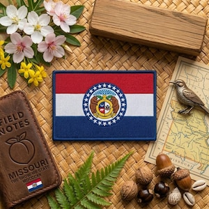 May include: A rectangular patch featuring the Missouri state flag, with red, white, and blue stripes and a central emblem. The patch is surrounded by a variety of natural elements, including flowers, nuts, and a small map.