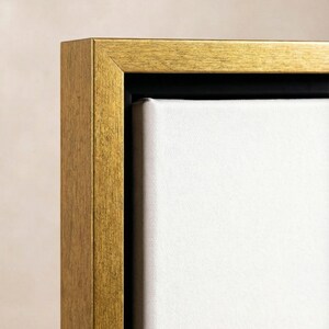 Puede incluir: Primer plano de un marco de fotos rectangular dorado con un lienzo blanco. El marco tiene una superficie texturizada y un interior negro. La obra de arte es probablemente una pintura o una impresi&oacute;n.