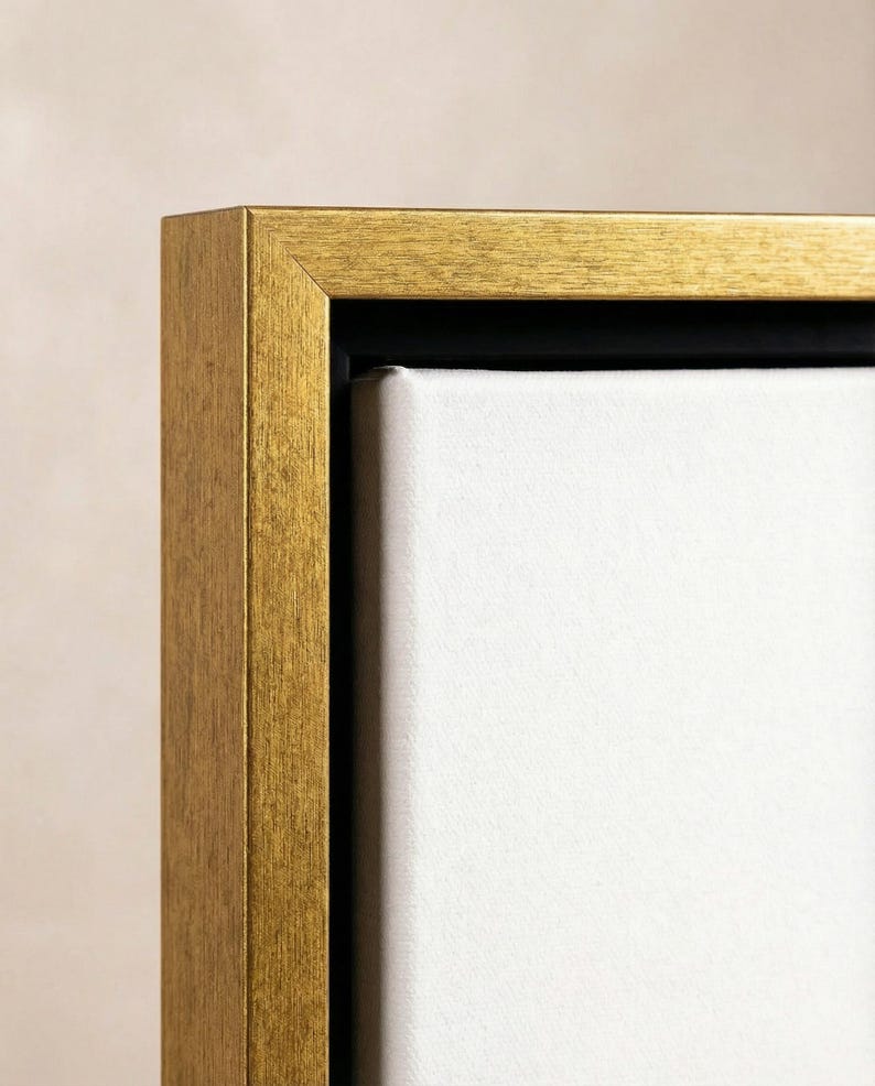 Puede incluir: Primer plano de un marco de fotos rectangular dorado con un lienzo blanco. El marco tiene una superficie texturizada y un interior negro. La obra de arte es probablemente una pintura o una impresi&oacute;n.