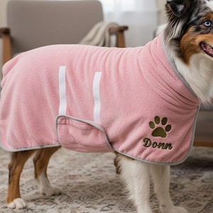 May include: A pink dog towel with white stripes and gray trim. The towel has a paw print and the name "Donn" embroidered in green. The dog is an Australian Shepherd with blue eyes.