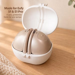 May include: A white, oval-shaped, hinged storage case containing two beige, dome-shaped breast pumps. The case lid is open, and the text "Made for Eufy S1 & S1 Pro. A cozy, protective home for your pumps" is printed on the upper left side of the image.