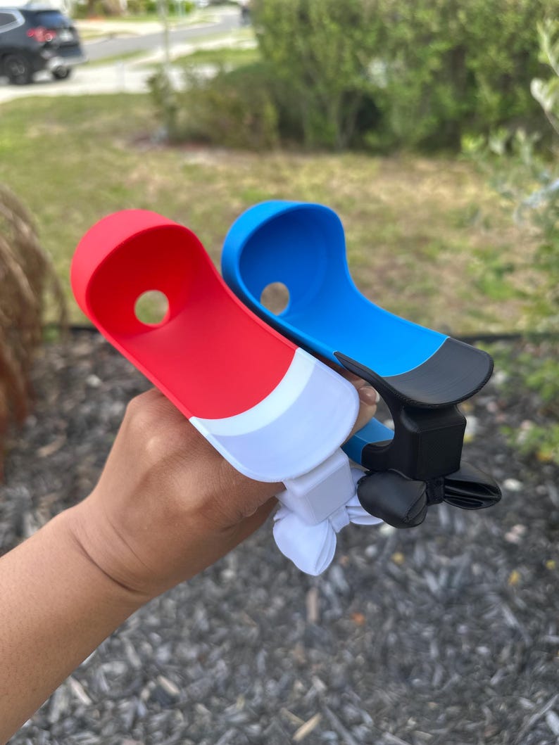 May include: Two plastic boat-shaped accessories, one red and white, the other blue and black. Each has a hole and a clip-like mechanism. The accessories are held up against a blurred outdoor background.