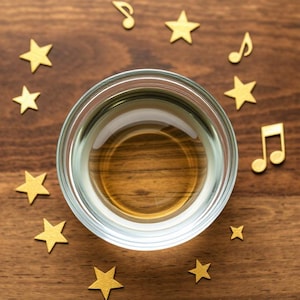 Puede incluir: Un vaso de vidrio transparente con un líquido dorado en su interior, rodeado de estrellas doradas y notas musicales sobre una superficie de madera.