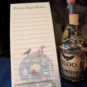 Può includere: Un blocco note bianco con le parole "Ingredienti della pozione" e un'illustrazione decorativa di un corvo, un cappello da strega e bottiglie di pozione. Una bottiglia decorativa con l'etichetta "Floo Powder" è accanto al blocco note.