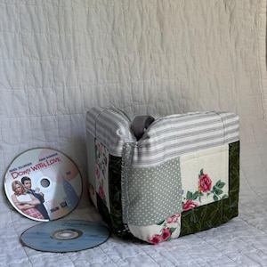 May include: A patchwork fabric tote bag with a gray handle. The bag features various fabric patterns, including floral, polka dot, and striped designs. Two DVDs are next to the bag. One DVD has the text "Down With Love".