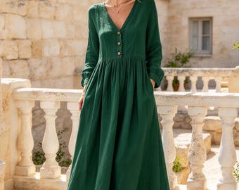 May include: A long-sleeved, floor-length dress in a deep forest green color. The dress features a V-neckline, a button-down front placket with three visible buttons, a gathered waistline, and a full, flowing skirt that reaches the ankles.