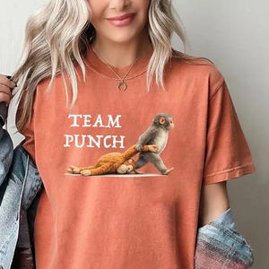 May include: Burnt orange t-shirt with the text "TEAM PUNCH" and a graphic of a monkey pulling another monkey. The shirt is a comfortable, casual style.
