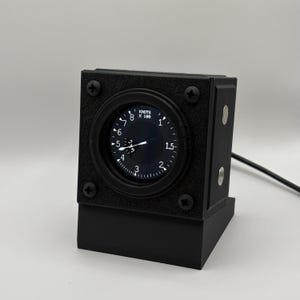 May include: A black, square-shaped aviation instrument gauge mounted on a matching stand. The circular display features a white needle and numerical markings with the text KNOTS X 100. Four black screws secure the faceplate to the housing.
