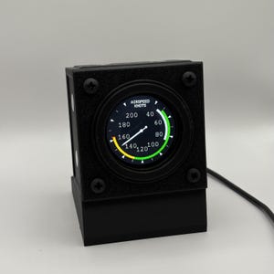 May include: A black, rectangular flight instrument gauge with a circular digital display showing airspeed in knots. The screen features a white needle, numerical markings from 40 to 200, and a green and yellow arc. Four black screws secure the faceplate.